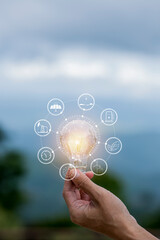 hand holding light bulb against nature, icons energy sources for renewable,