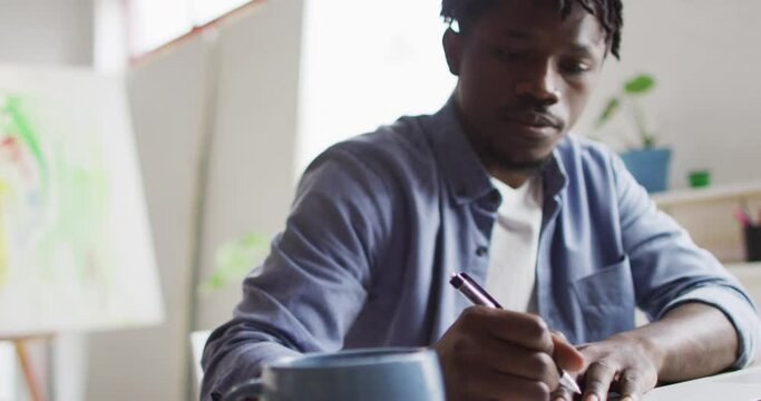 African american male artist taking notes while sitting on his desk at art studio