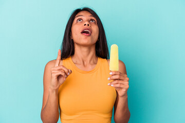 Young latin woman holding ice cream isolated on blue background pointing upside with opened mouth.