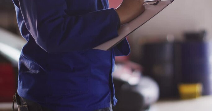 Mid section of female mechanic taking notes on clipboard at a car service station