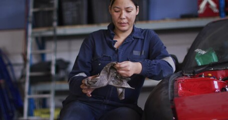 Portrait of female mechanic cleaning her hands with a cloth sitting at a car service station - Powered by Adobe