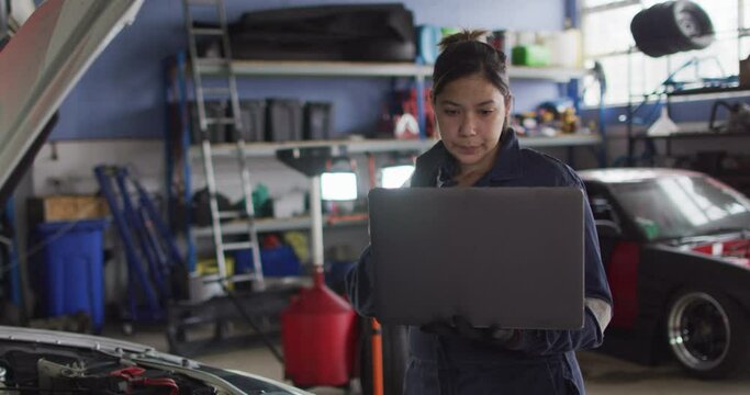 Female mechanic using laptop and inspecting the car at a car service station