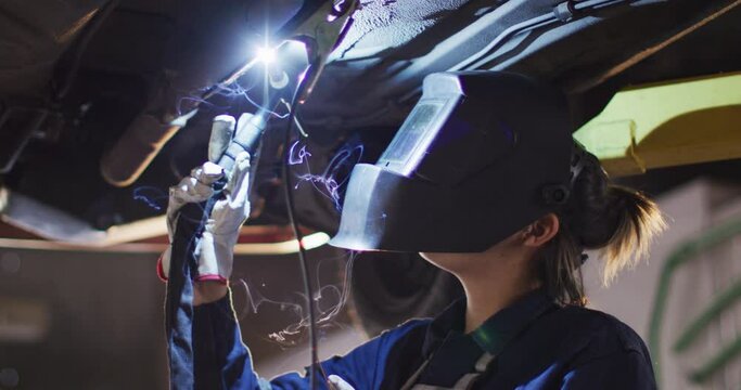 Female mechanic wearing welding helmet welding under a car at a car service station