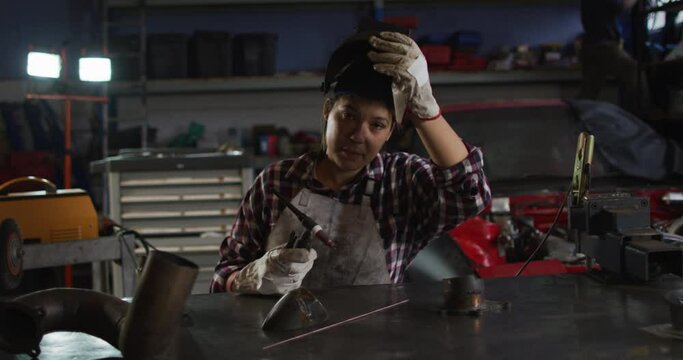 Portrait of female mechanic removing welding helmet while sitting at a car service station