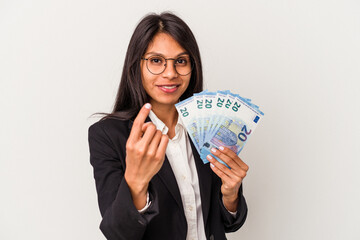 Young business latin woman holding bills isolated on white background pointing with finger at you as if inviting come closer.