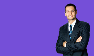 Portrait of happy smiling brunette businessman in black suit, white shirt and blue stripes tie, standing in crossed arms pose, over violet purple background with copy space. Confident business man.