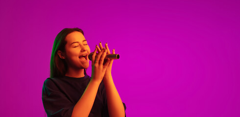 Flyer with portrait of pretty young caucasian girl singing into microphone isolated over pink background in neon lights