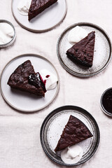 Slices of rich moist chocolate cherry cake. Homemade dark chocolate sweet brownies cakes with ice cream on greige linen tablecloth. Selective focus