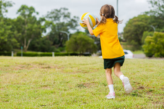 School girl running and catching ball on green grass at school PE
