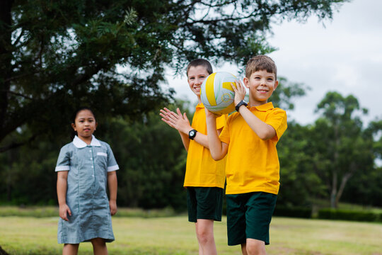 Happy healthy school kids throwing a ball to one another outside