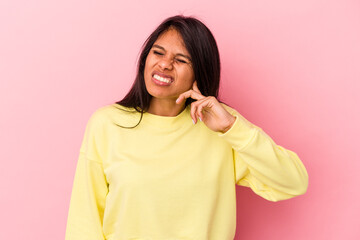 Fototapeta premium Young latin woman isolated on pink background covering ears with fingers, stressed and desperate by a loudly ambient.