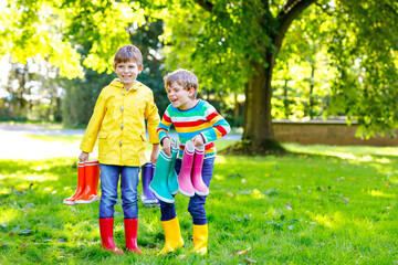 Fototapeta premium Two little kids boys, cute siblings with lots of colorful rain boots. Children in different rubber boots and jackets. Footwear for rainy fall. Healthy twins and best friends having fun outdoors