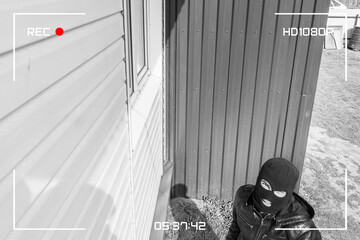 A man in a black mask is trying to rob a house. There is recording on an outdoor video surveillance camera. The robber noticed a security camera. Robbery of a private house. Criminal concept - obrazy, fototapety, plakaty