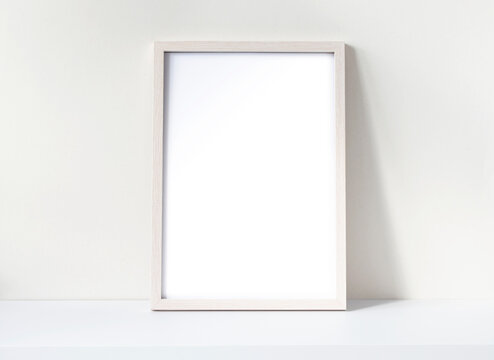 Photo frame mockup with white blank sheet on a white desk. Pine wooden frame mockup. Space for text.