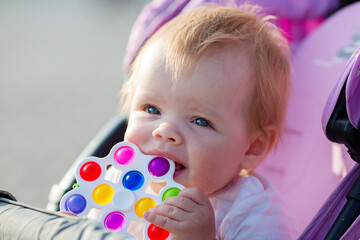 A smiling child in a baby carriage with bright toy on a walk.