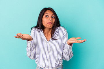 Young latin woman isolated on blue background doubting and shrugging shoulders in questioning gesture.