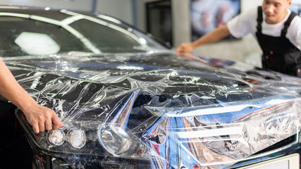Two technician worker wrapping vehicle hood using protector vinyl plastic wrap for protect car painting from scratch.