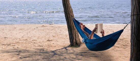 Fototapeta premium man reading a book in a hammock by the sea
