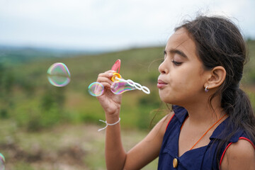 Young girl kid playing by blowing soap water bubbles - conept of playful chidlren during holiday...