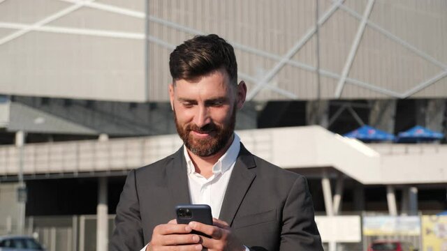 Bearded Confident Businessman Checking Mails on Smartphone. Satisfied Young Office Worker using Mobile Phone Outside. Reading News, Typing Message in Online Chat. Applications for Business. 