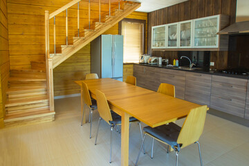Kitchen interior with great design. Modern kitchen with wood furniture. Kitchen interior with brown cabinets and table. Interior in dining room. A village staircase leads to second floor.