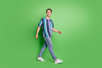 Fototapeta na wymiar Full length photo of charming happy young man walk empty space good mood weekend isolated on green color background