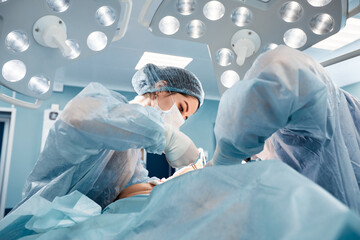Surgeons men and women in one team during an operation over the operating table, doctors in modern...
