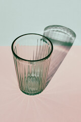 Green drinking glass with harsh shadow on colored background.
