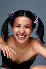 Portrait of a beauty asian girl smiling at the camera, a beautiful female face with clean and healthy skin, dark hair with pigtails, close-up on a gray background