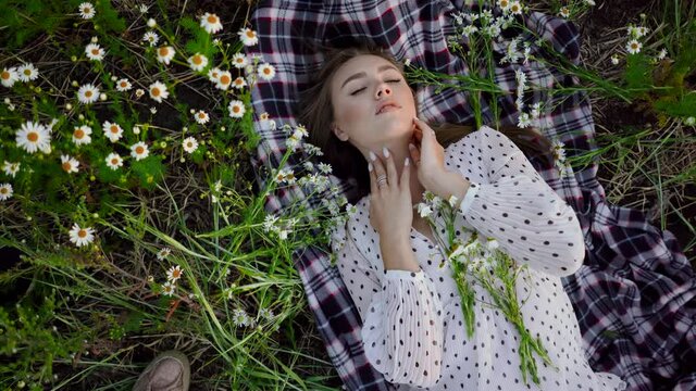 A first-person view of a photographer taking pictures of a beautiful young woman lying on the grass among daisies and posing.