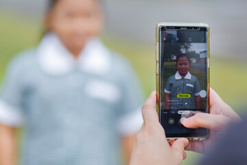 Mum holding mobile phone to take photos of her daughter on first day back to school