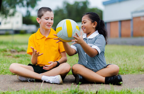 Aussie Boy and girl in playground at primary school throwing ball to each other