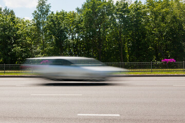 The motion of a blurred car along the street in the daytime.