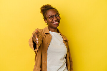 Young african american woman isolated on yellow background stretching hand at camera in greeting gesture.