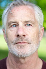 Handsome blue eyed senior male with grey hair and beard in park. Closeup