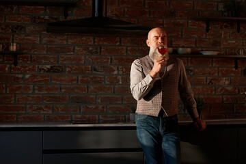 handsome man looking at the red wine in his glass .