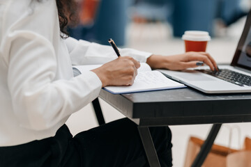 woman using a laptop and taking notes in a notepad .