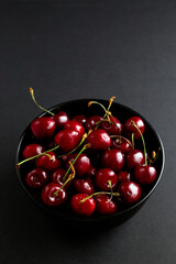 red sweet cherry in black plate on grey background