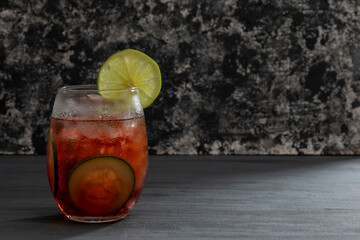 Bebida o Coctel con agua mineral, hielos y pepinos en rodajas sobre una mesa negra