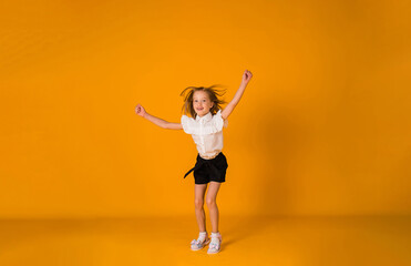 a cheerful schoolgirl in a uniform jumps on a yellow background with a copy of the space