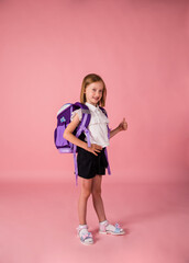 a schoolgirl in uniform and with a full-length backpack shows a class on a pink background with a copy of the space with her hand