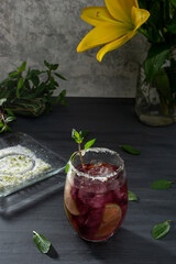 Bebida escarchada con hielos y rebanadas de limón, sobre una mesa color gris y un florero con flores amarillas