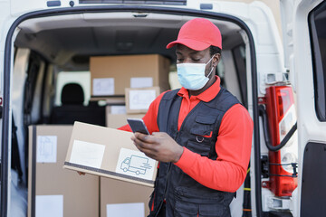 African american delivery man with smartphone holding package while wearing safety face mask for coronavirus outbreak