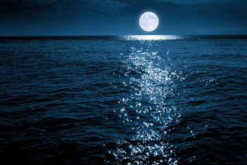 This large full blue moon rises brightly over the calm ocean creating sparkles across the waves - 445195961