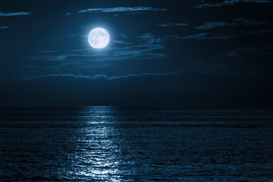 This large full blue moon rises brightly over the cloud bank in this calm ocean