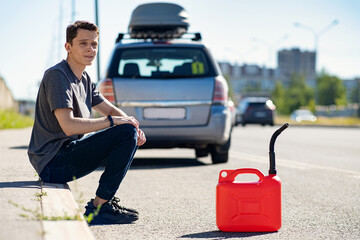 A red canister on the asphalt near the car. The car ran out of gas and stalled. A young man hoping for help on the road from other drivers.