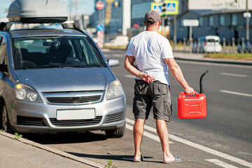 A red canister on the asphalt near the car. The car ran out of gas and stalled. A young man hoping for help on the road from other drivers.