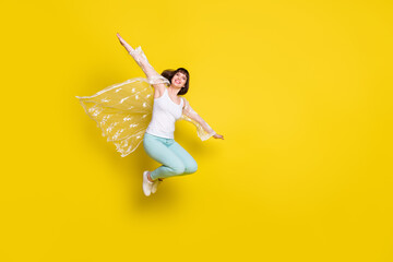 Full body photo of attractive young cheerful woman jump up plane wings hands isolated on yellow...