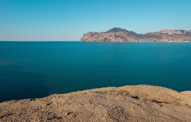 The edge of the mountain cliff. A mountain peak. A steep cliff on the sea coast. A steep mountain on the background of a clear sky and ocean.