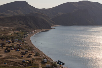 Camping on the beach. A tent city in a quiet bay on the coast and against the backdrop of mountains.